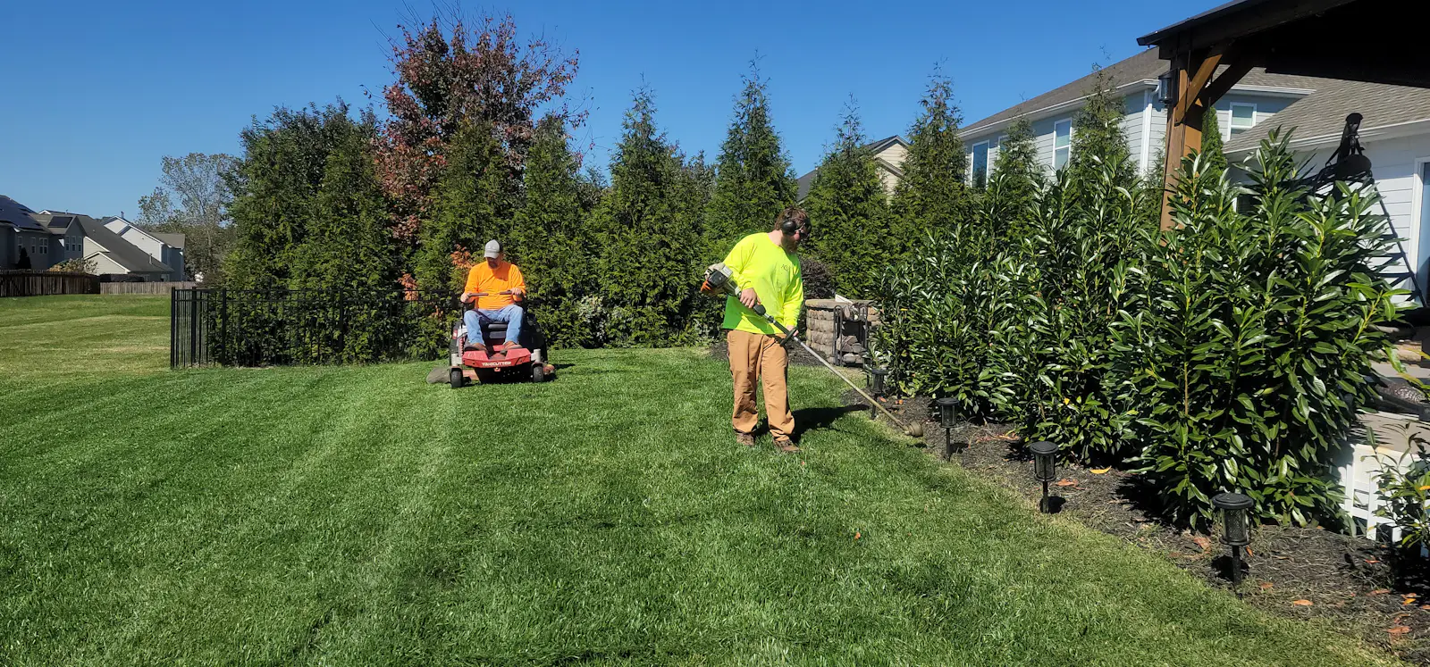 A crew member mows a wide green lawn with a walk-behind mower